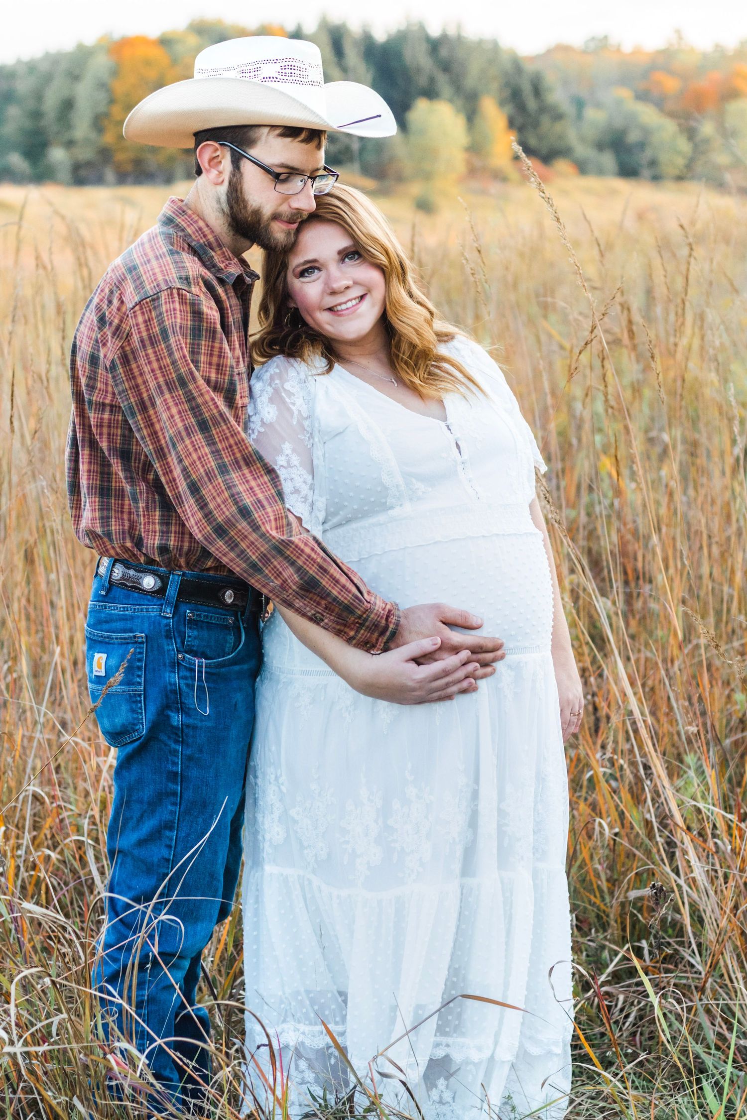 Country-style maternity photo of couple in wheat field during golden hour.