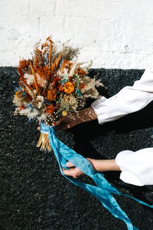 A dried flower bouquet with orange and blue tones held against a white wall.