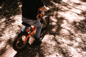 Child's legs riding an orange balance bike on a dappled sunlit path.