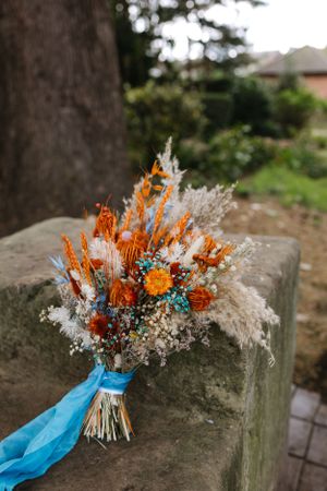 A stunning wedding bouquet with orange flowers and dried pampas grass tied with a blue ribbon.