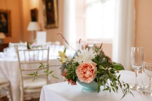 Vintage-inspired floral centerpiece with coral roses in a turquoise vase on a white tablecloth.