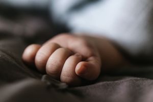 Close-up of a tiny infant hand resting on soft fabric in muted lighting.