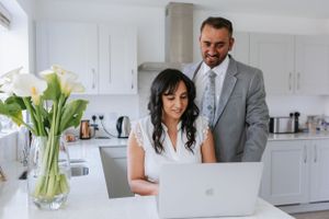 Couple working together on laptop in modern white kitchen with fresh flowers.