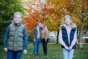 A group stands together outdoors during autumn with colorful fall foliage of orange and red maple trees in the background.