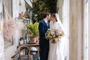 A wedding couple shares a romantic moment in a rustic garden setting with lush floral bouquet.