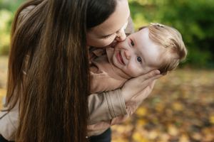Parent sharing playful moment with laughing baby in autumn outdoor setting.