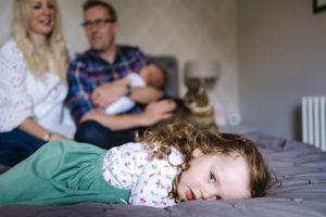 A young child rests on green bedding while others sit in background.