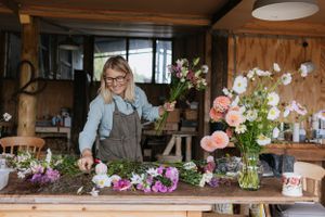 Florist arranging fresh flowers in mason jars on a rustic wooden workbench.