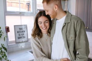 Couple sharing intimate moment while laughing together in bright kitchen.