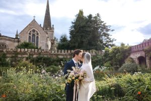 A wedding couple shares an intimate moment in front of a historic stone church with traditional spire.