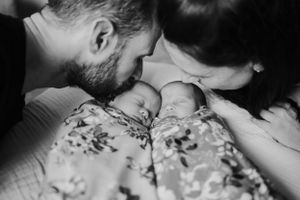 Black and white intimate photo of parents lovingly embracing their sleeping newborn twins.
