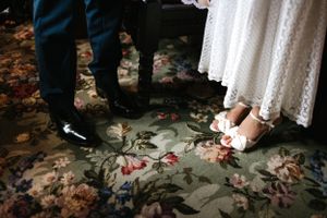 Close-up of wedding shoes on a floral patterned carpet during the ceremony.