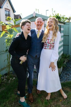 Three people share a joyful laugh together in a backyard garden setting.