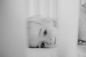 Close up black and white portrait through crib bars showing soft lighting and gentle expression.