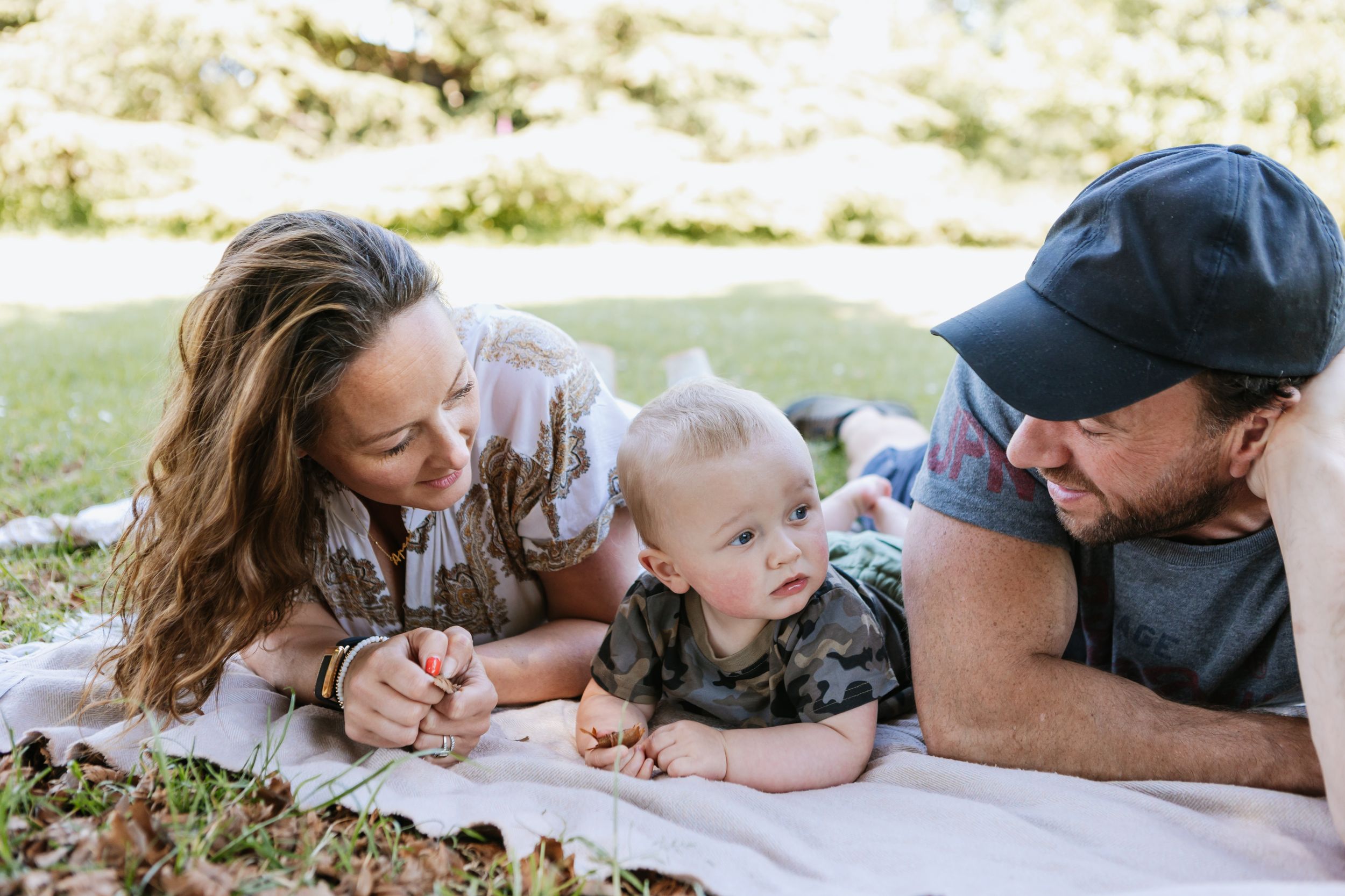Family lying on blanket outdoors enjoying quality time together.