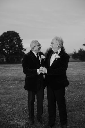 Black and white photo of two elderly men in suits sharing a joyful moment outdoors.