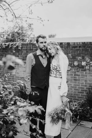A couple poses against a brick wall in a garden setting.