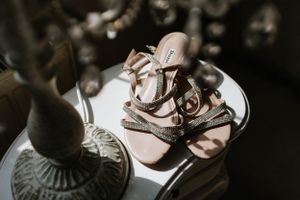 Delicate pink sandals with bow details displayed on reflective surface.