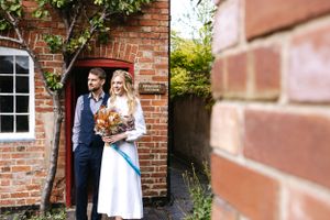 A couple stands in a doorway of a rustic brick building with climbing vines.