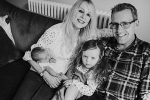 A family relaxes together on a dark couch in their living room.