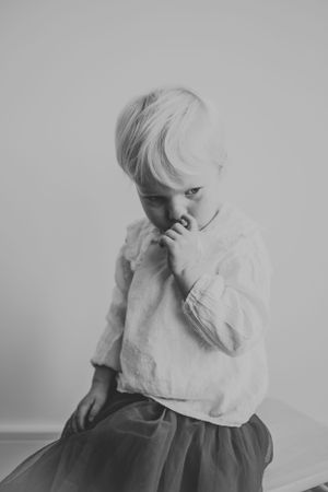 Black and white portrait of young child in light colored clothing against minimal background.