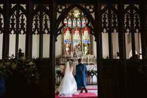 Church wedding ceremony view through ornate gothic archway with stained glass windows.