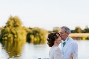 A tender moment between a couple against a sunlit lake backdrop during their wedding celebration.