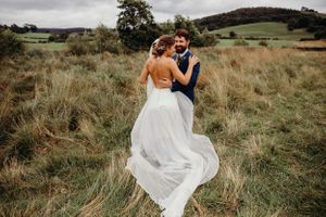 A romantic wedding couple embraces in a windswept meadow with rolling hills in the background.