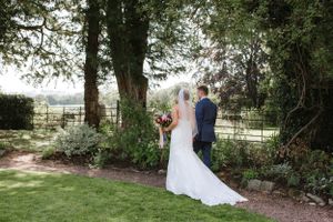 Newlywed couple standing under trees at outdoor garden wedding venue.