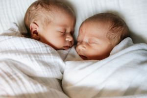 Two sleeping newborn babies lying peacefully side by side on white bedding.