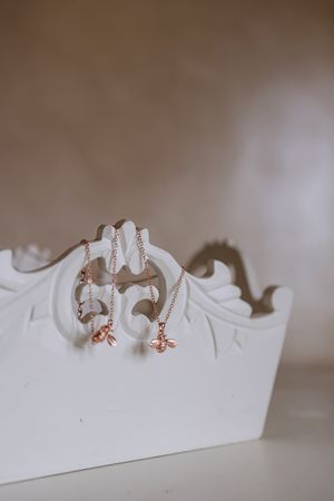 Close-up of dainty rose gold bee earrings on white display.