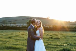 A newly married couple embraces in a sunlit meadow at golden hour.