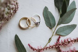 Wedding rings and eucalyptus leaves artfully arranged with dried flowers on white background.