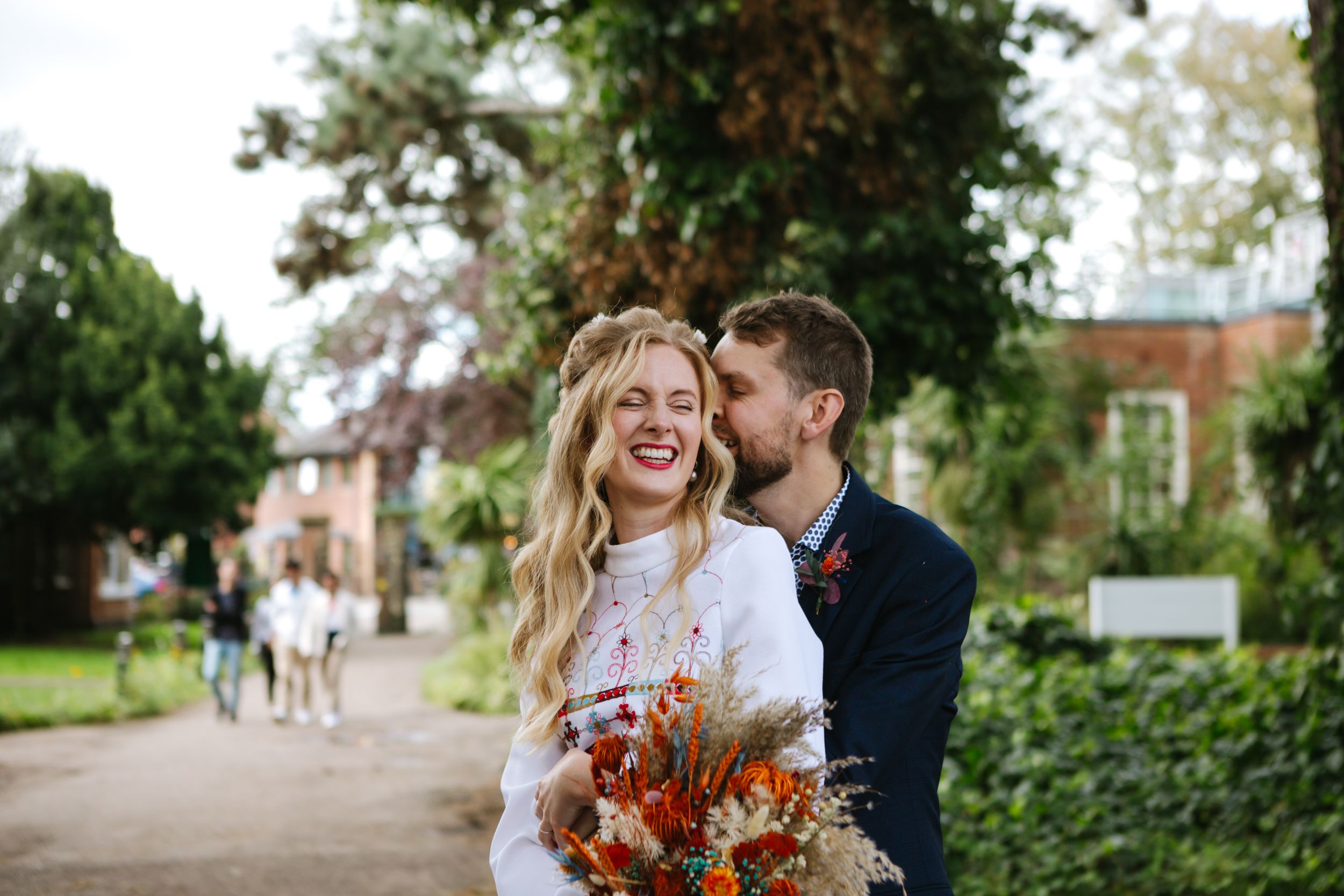 A candid wedding moment captured in a garden setting with a vibrant orange bouquet.