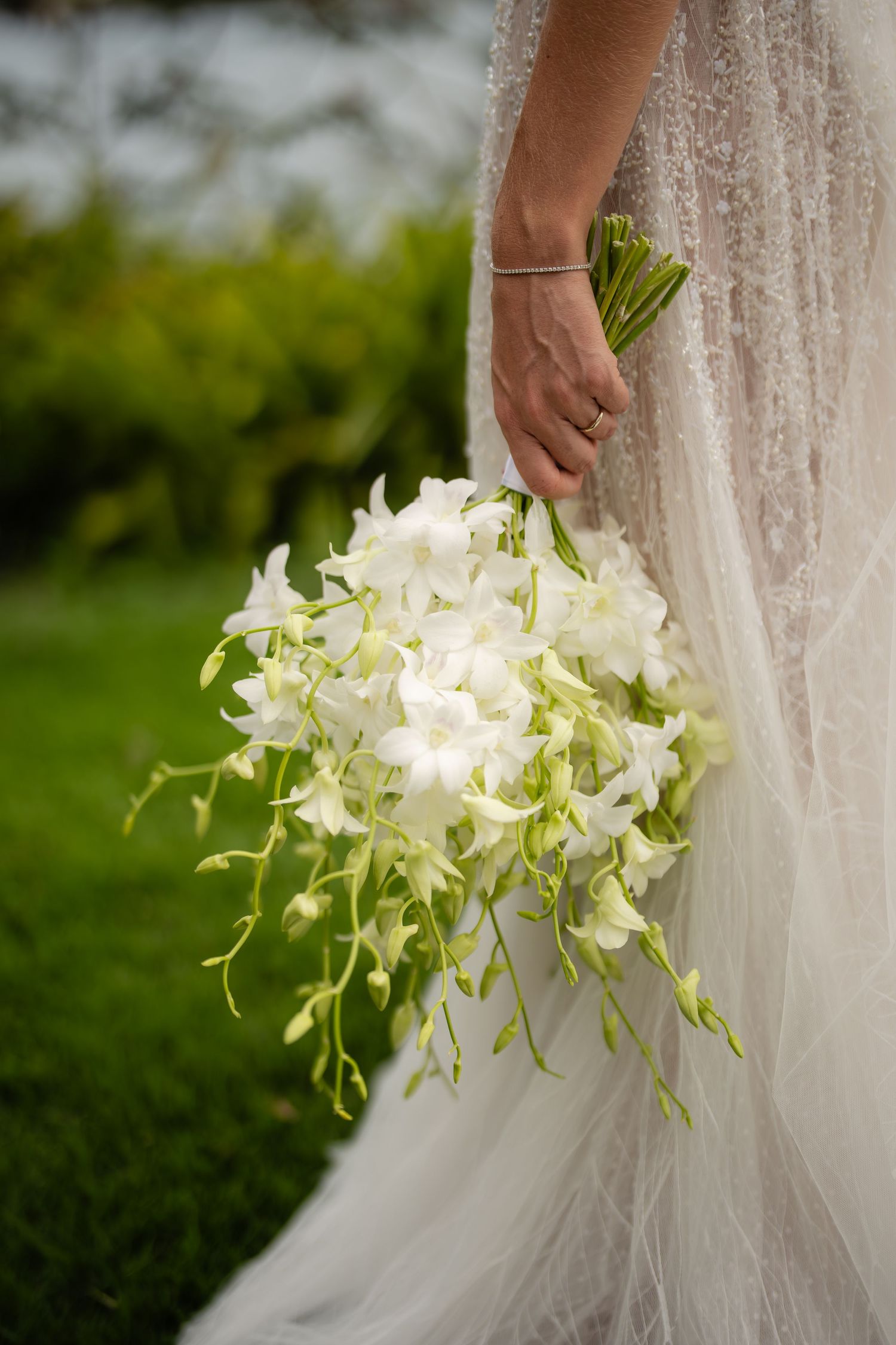 Elegant white orchid wedding bouquet held against a flowing tulle dress.