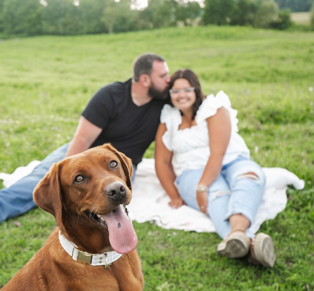 A photo of a dog with a couple behind it.