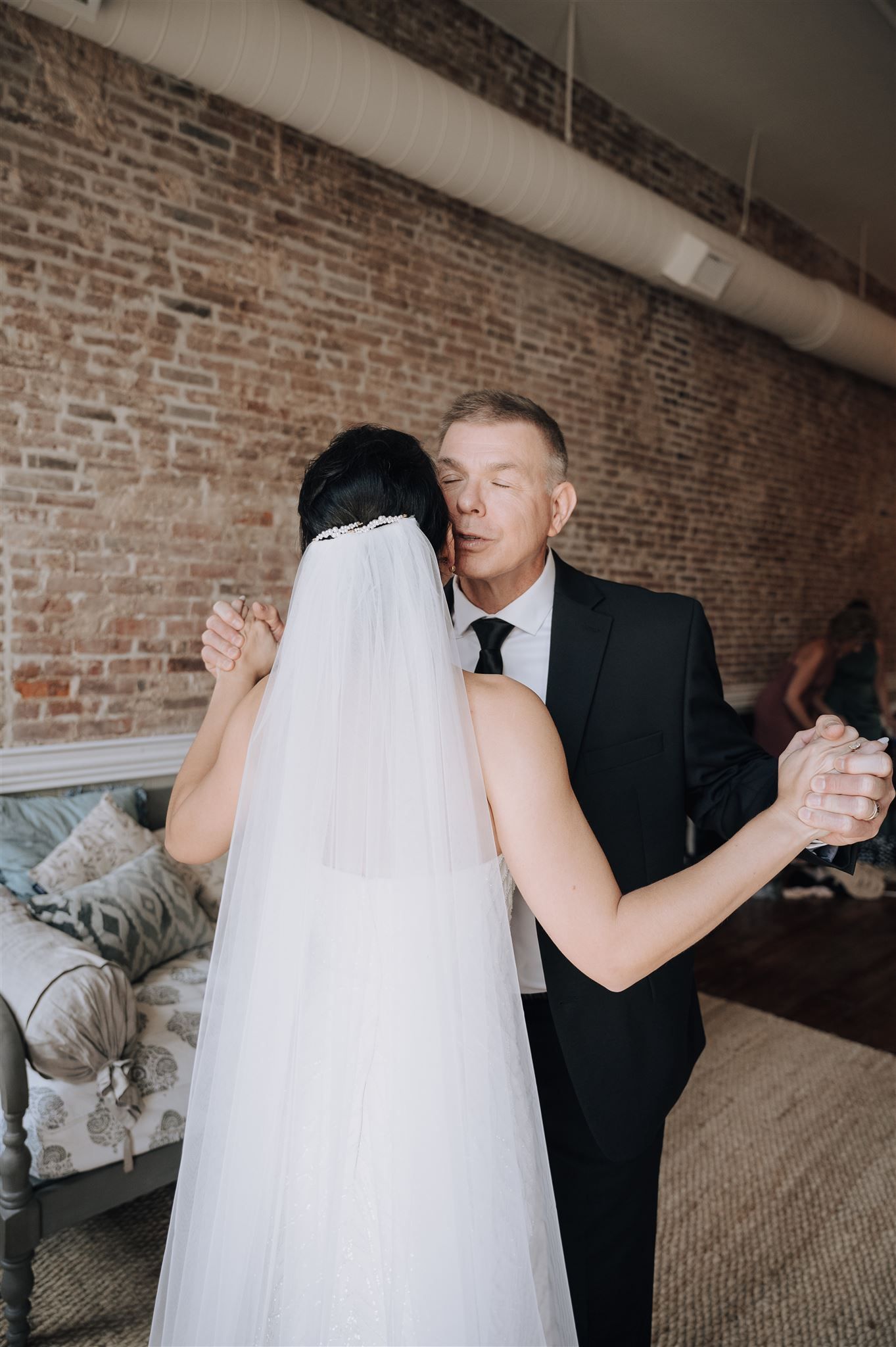A tender wedding day embrace captured against industrial brick backdrop.