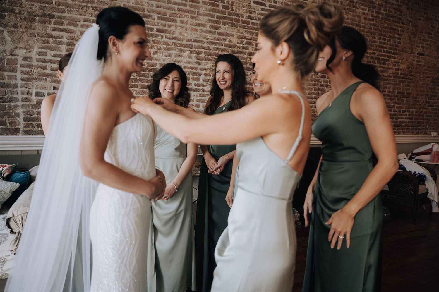 Wedding party shares intimate moment during preparation in rustic venue with exposed brick walls.