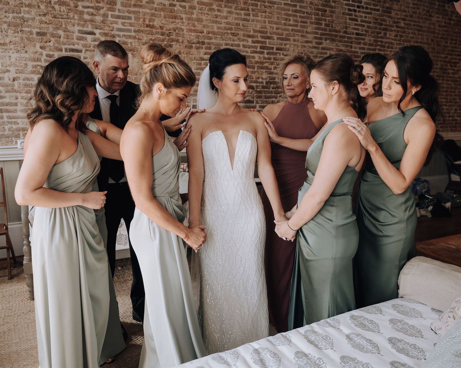Wedding party shares intimate moment in brick-walled room during pre-ceremony preparations.