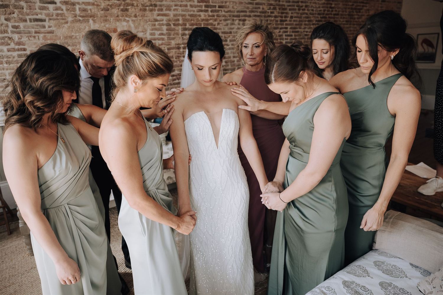 Bridesmaids in sage and neutral dresses gather around bride in elegant white gown.