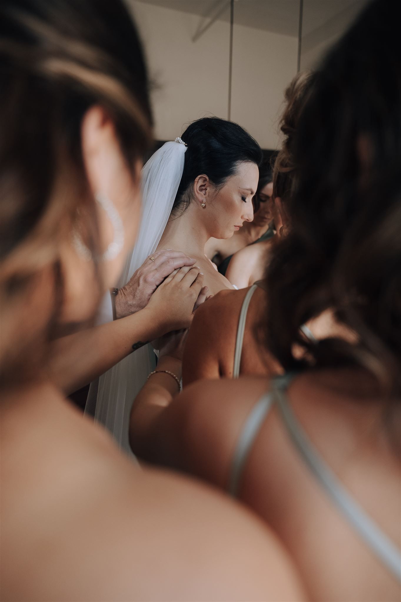 Tender moment during bridal preparations with bridesmaids surrounding in support.