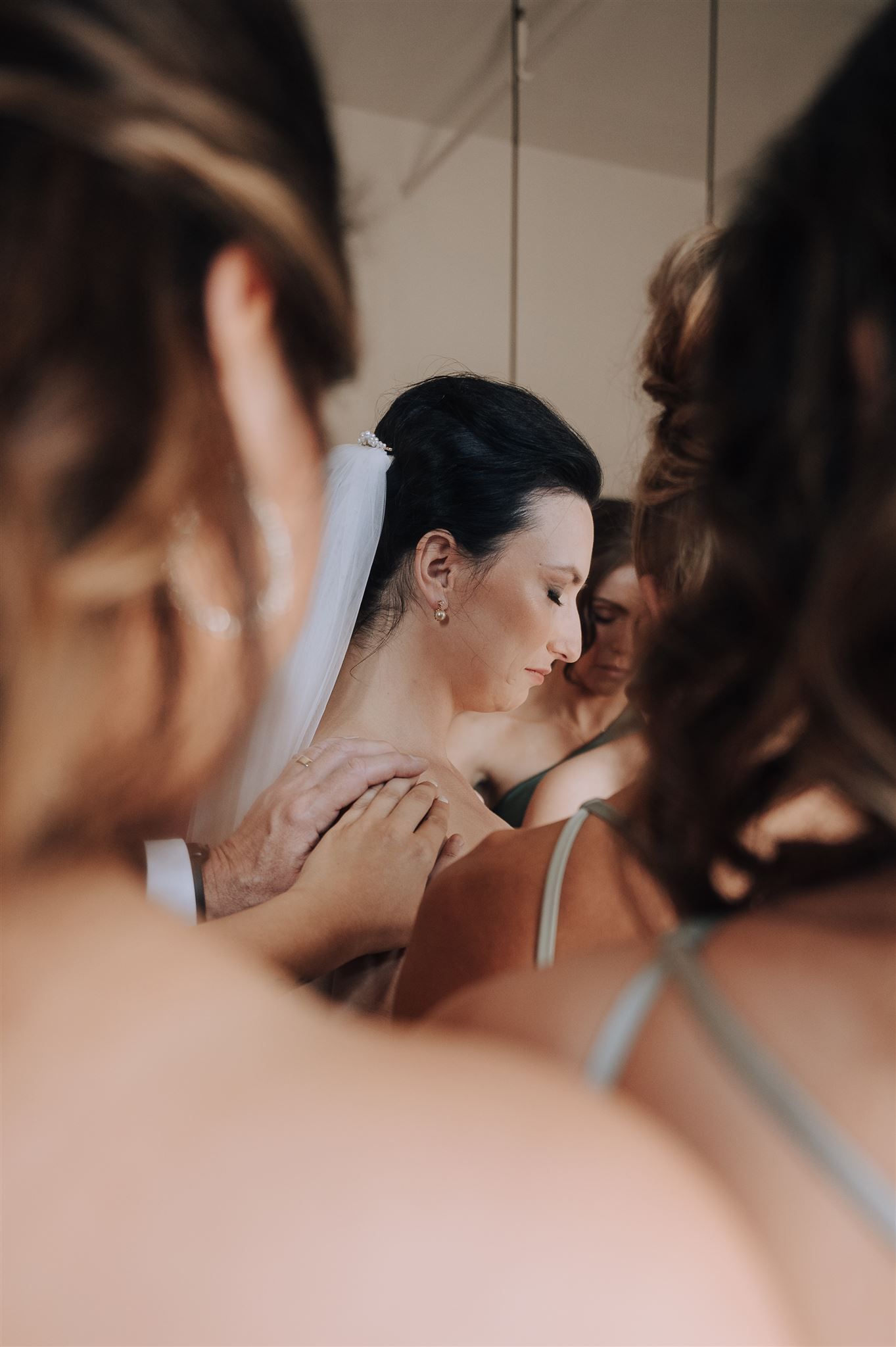 Emotional bridal preparation moment captured in intimate close-up with bridesmaids helping.