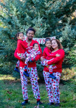 Family wearing matching Santa-themed pajamas poses together for Christmas photos outdoors.