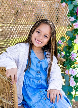 Portrait series showing a child in denim and white against a wicker chair backdrop with flowers.