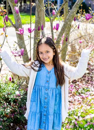 Springtime photos of a child in a blue dress and white sweater among blooming magnolia trees.