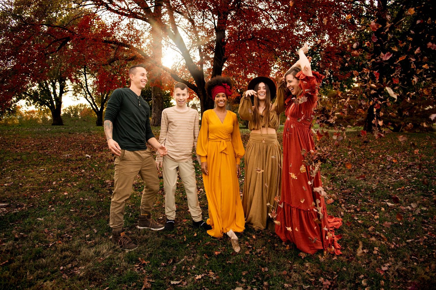 Family of five standing among vibrant red autumn trees tossing fall leaves in a park.