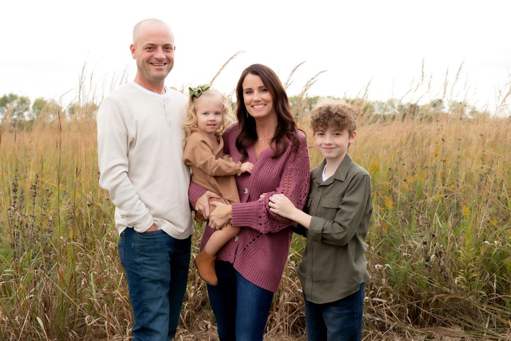 Family of four poses together in tall autumn grass during sunset.