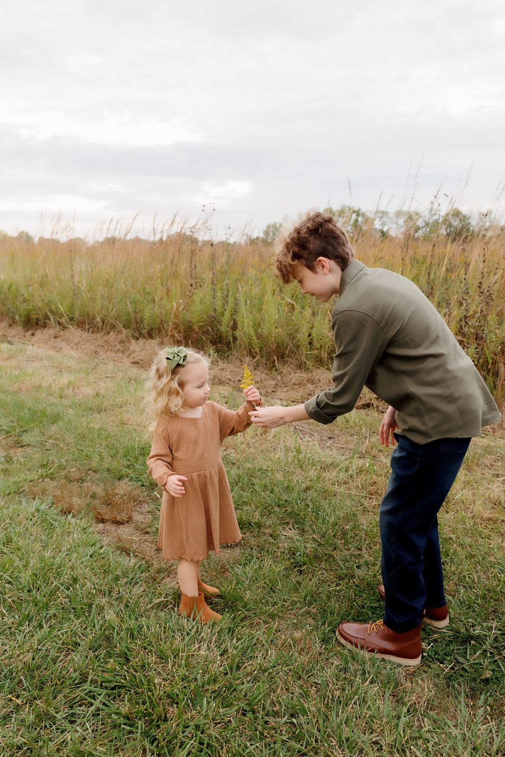 Adult and small child interact playfully in a field of tall grass during autumn.