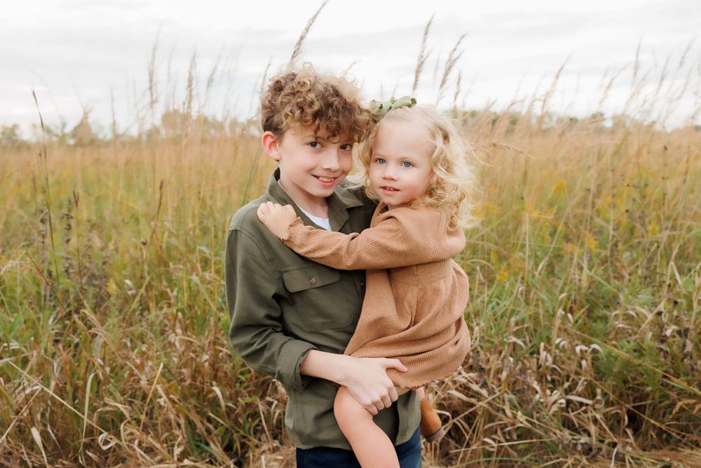 Two children share a sweet hug while standing in a golden field.