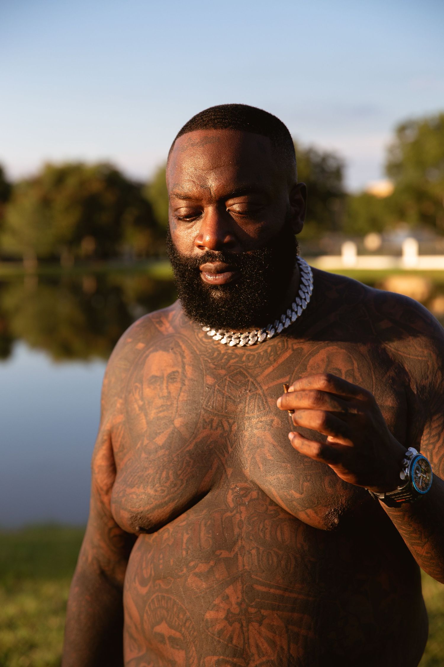 Rick Ross casually standing in front of a lake at his Atlanta estate.